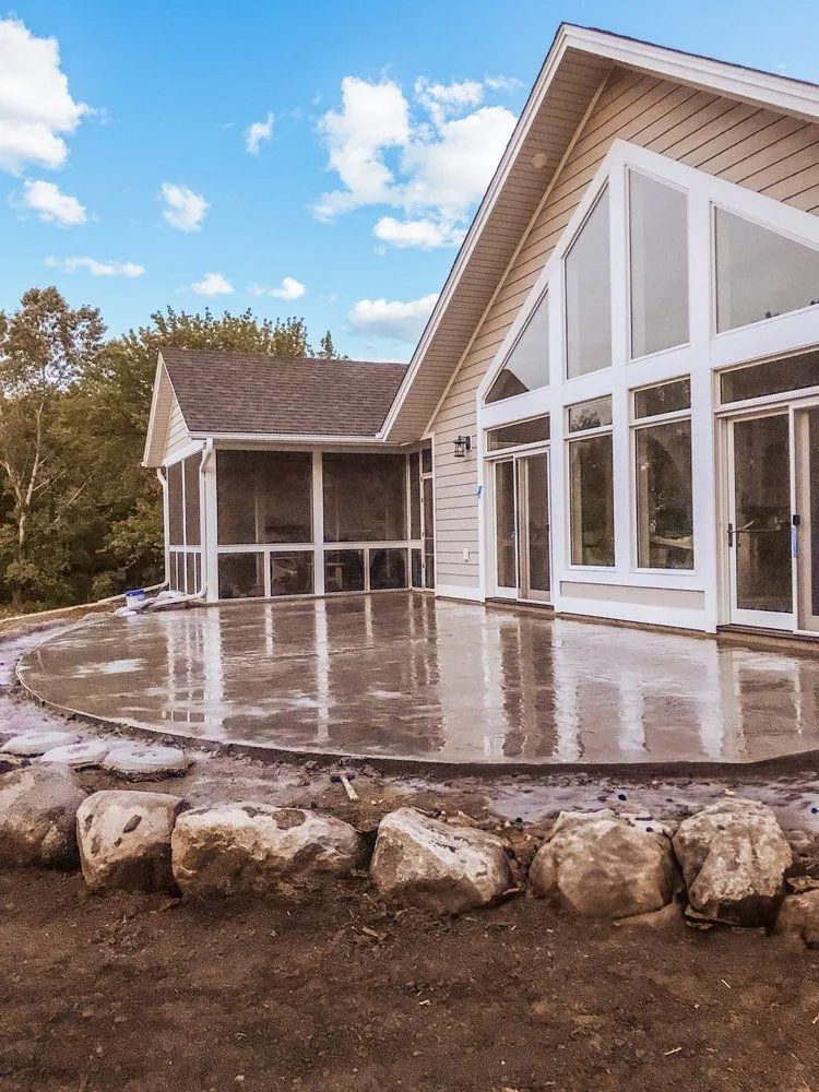 Large patio with boulders, screened porch, and house with large windows under a blue sky.
