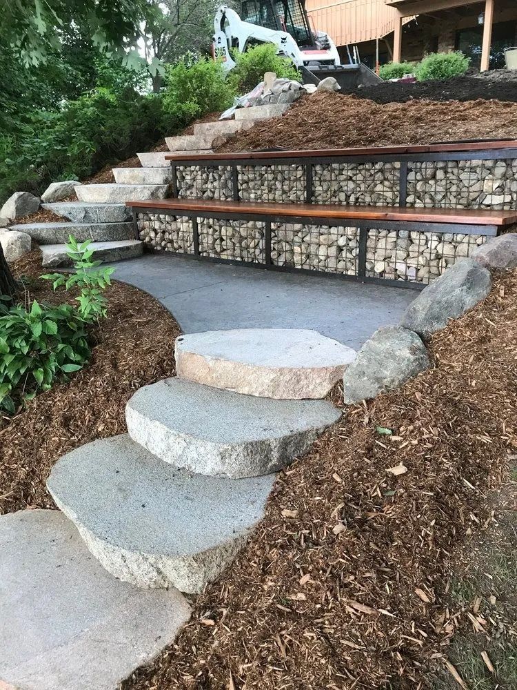 Stone steps and seating area built into a hillside, with gabion baskets filled with rocks.
