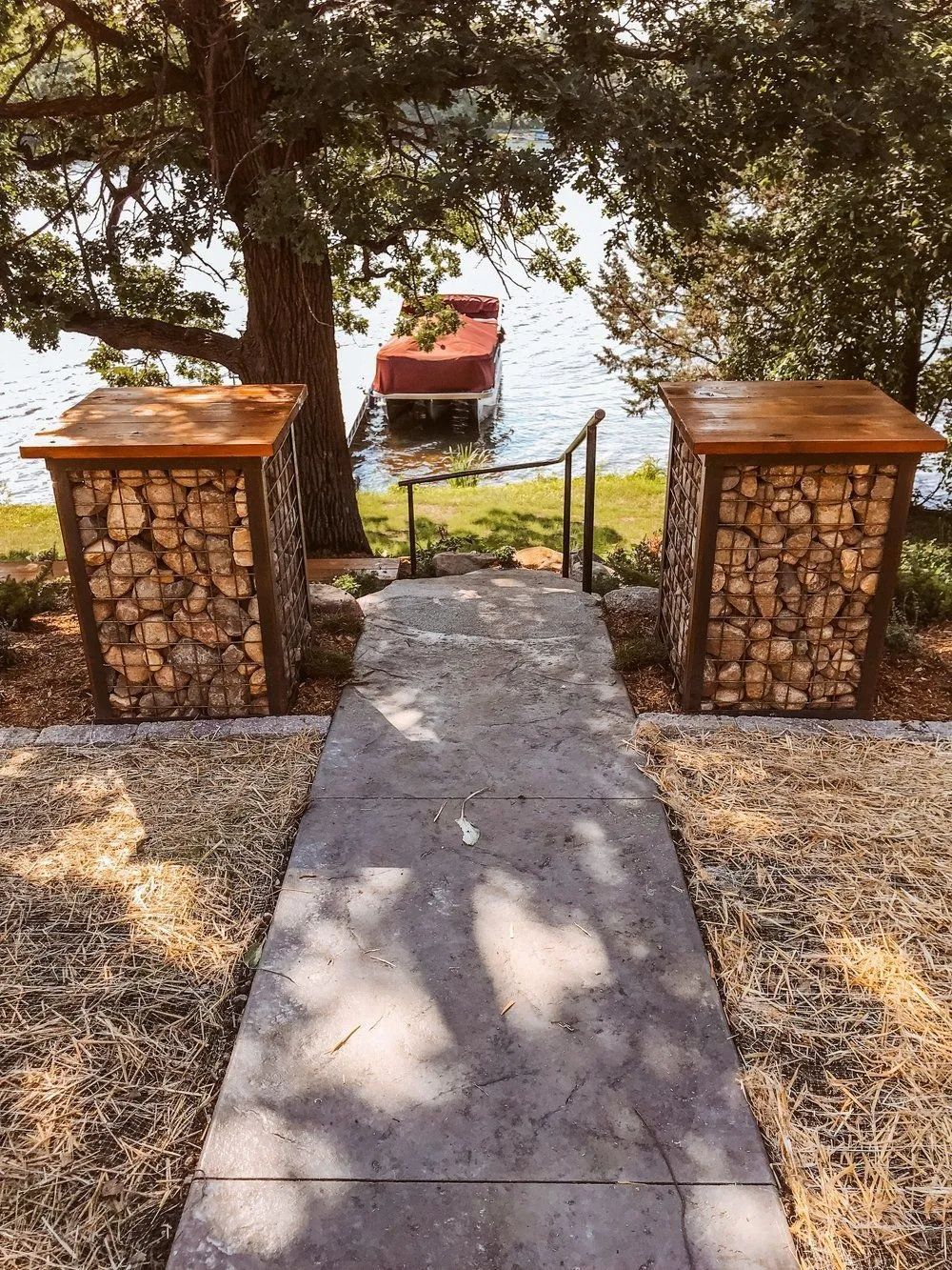 Concrete path leads to lake, flanked by stone columns, dock in the distance.