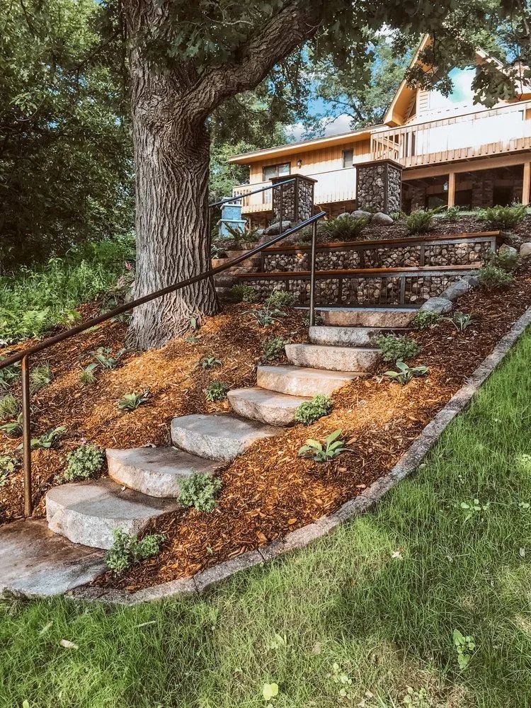 Stone steps leading up a hillside towards a building, with a railing and landscaping.