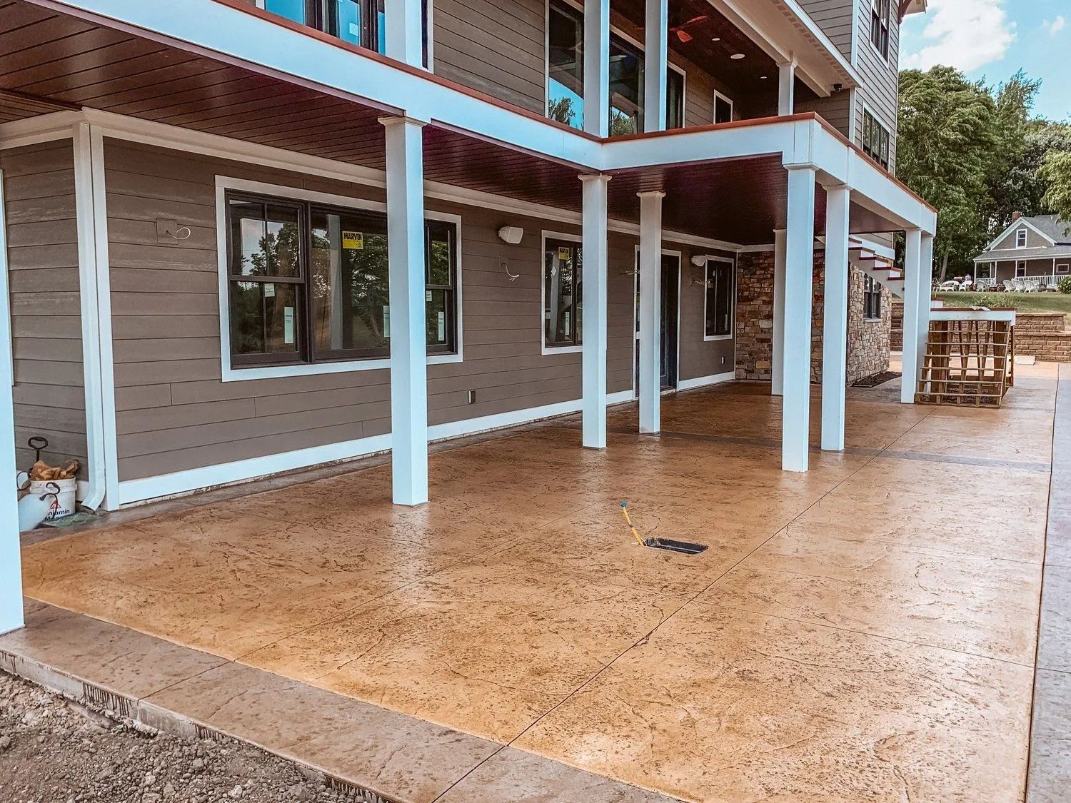 Tan concrete patio with white columns supporting a covered porch, brown house in background.