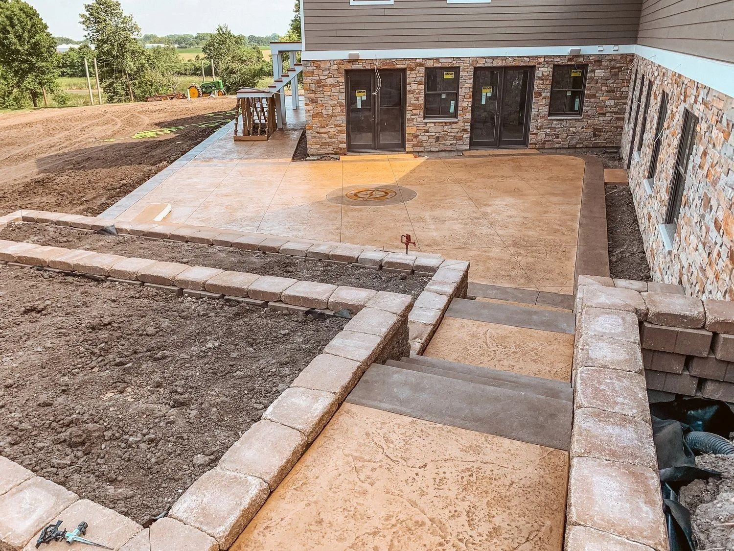Exterior view with steps leading down to a concrete patio, retaining walls and a building with stone and wood siding.
