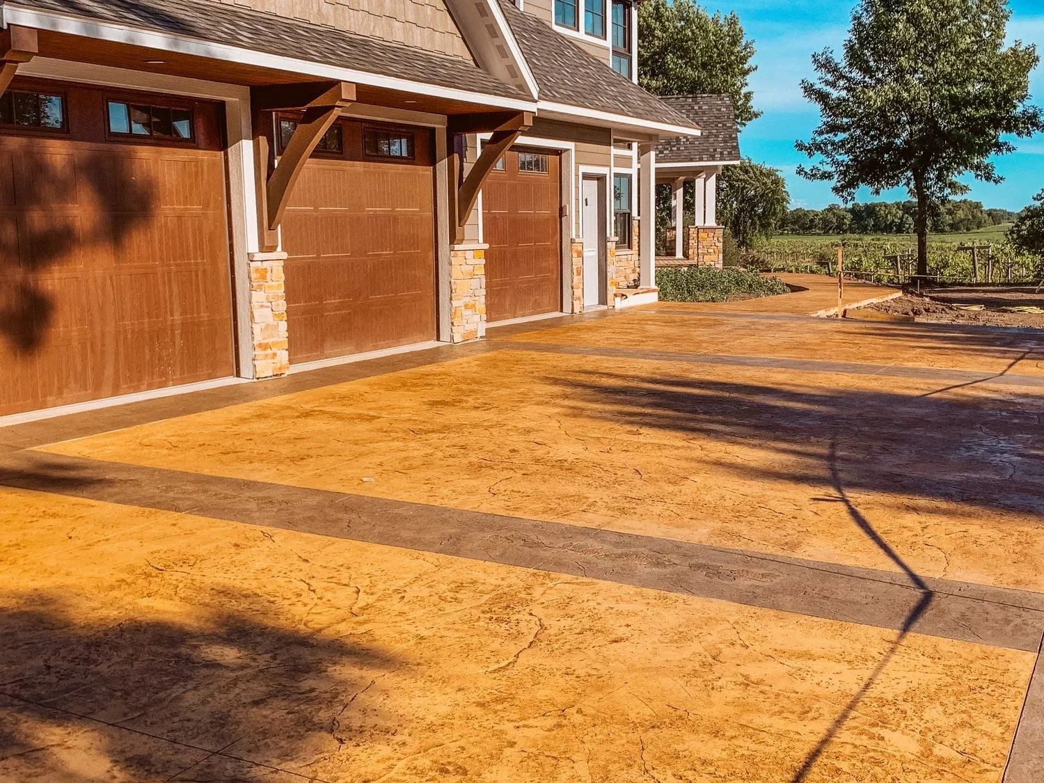 Brown garage doors and decorative concrete driveway lead to a house with a stone facade.
