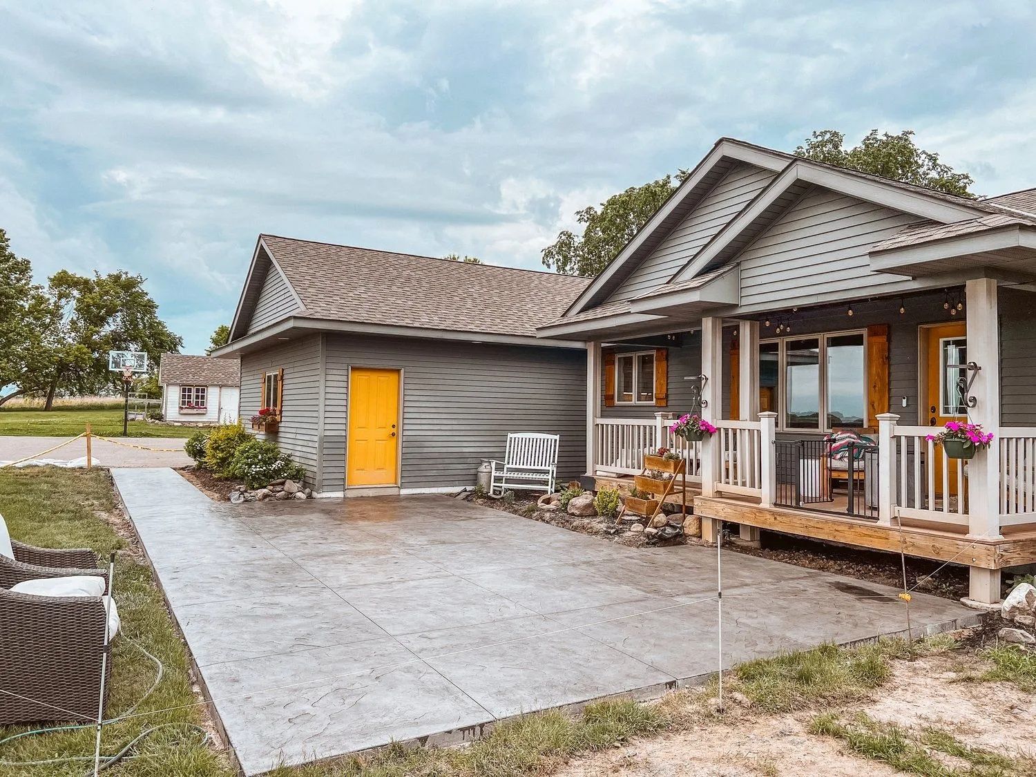 Gray cottage with yellow door, front porch, and concrete patio on a cloudy day.