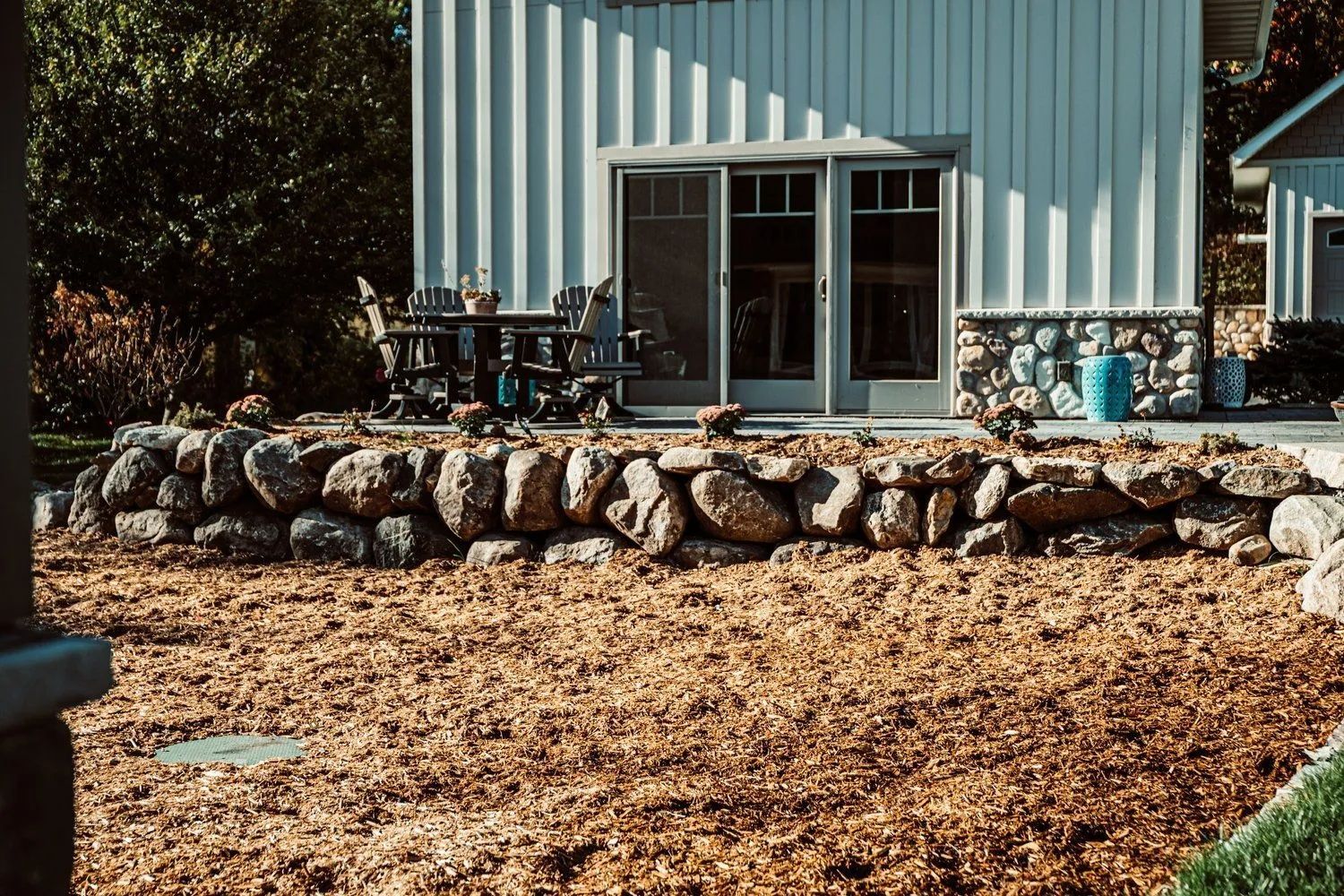 A building with white siding, stone base, and a rock retaining wall in front of a mulched yard.