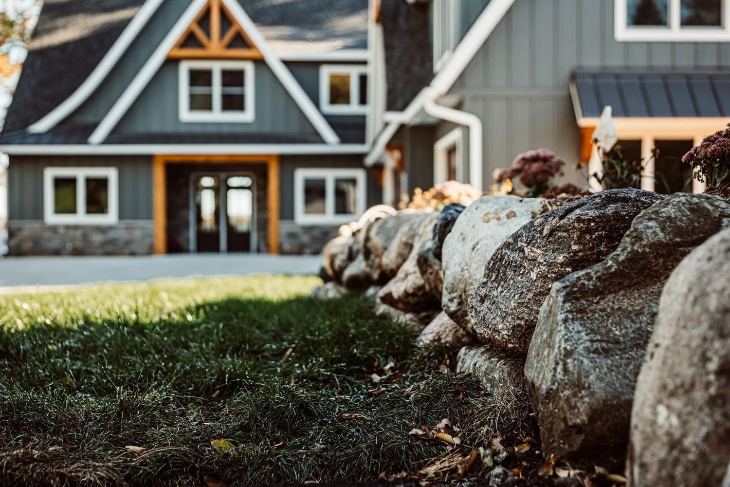 Gray house with white trim, wood accents, and a stone wall in front.