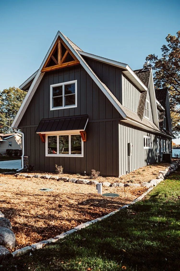 Gray and white A-frame house with a red awning, on a sunny day.