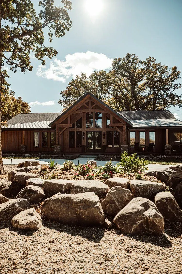 Wooden lodge with a large front entrance, surrounded by trees and a rock garden.