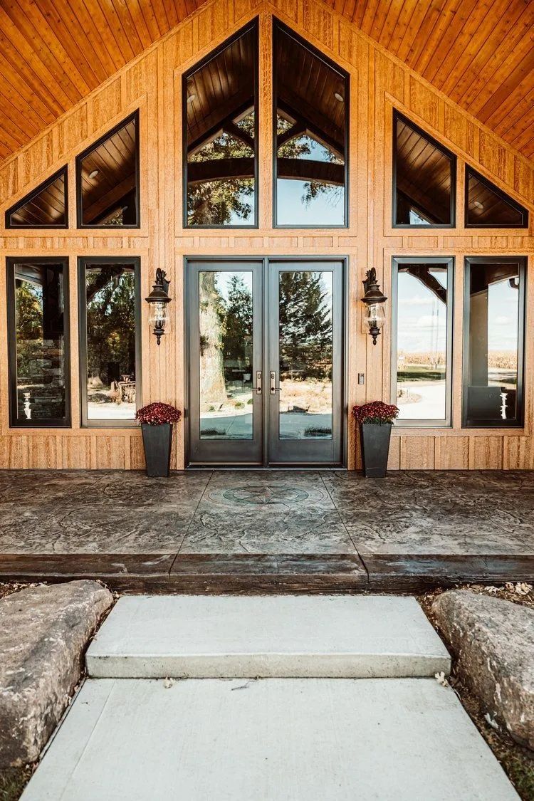 Wooden building entrance with glass doors, windows, and planters. Concrete steps lead up.