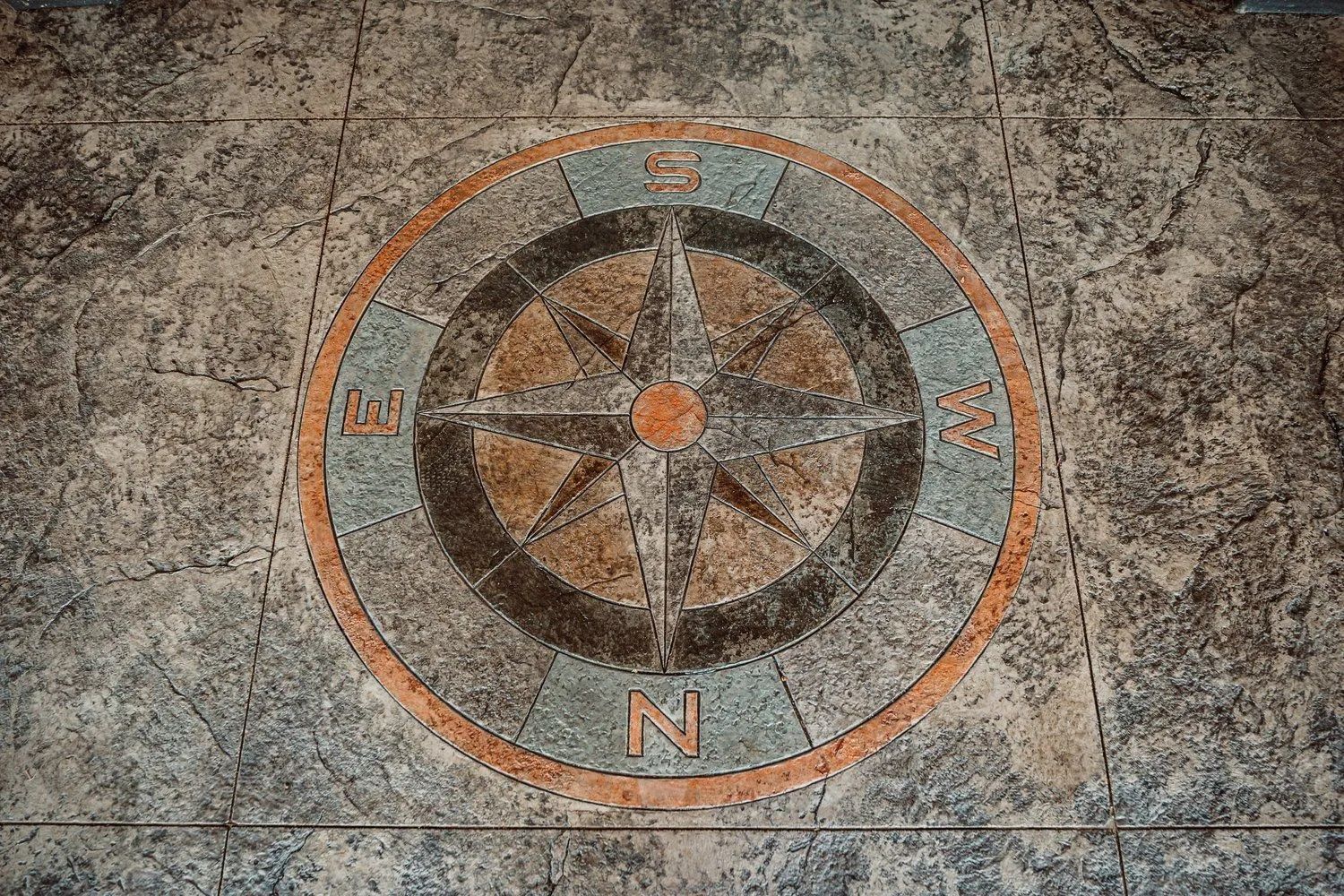 Compass rose design inlaid on a stone floor with shades of brown, orange, and blue.