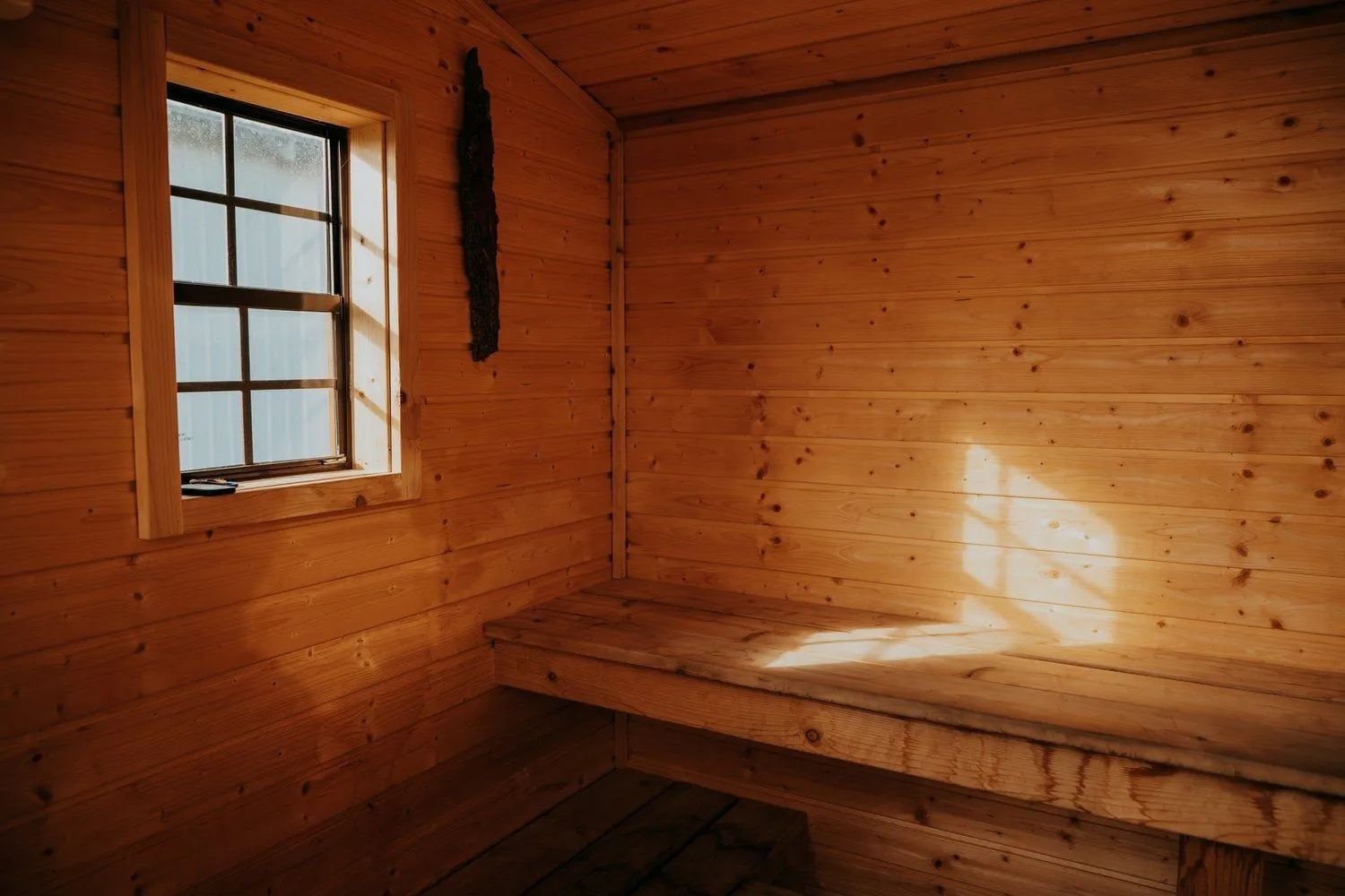 Wooden sauna interior with window, bench, and sunlight.