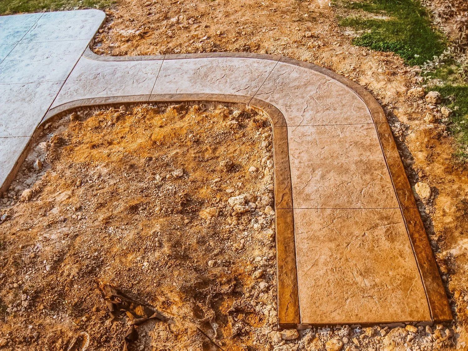 Concrete pathway under construction with a curved corner, surrounded by dirt.