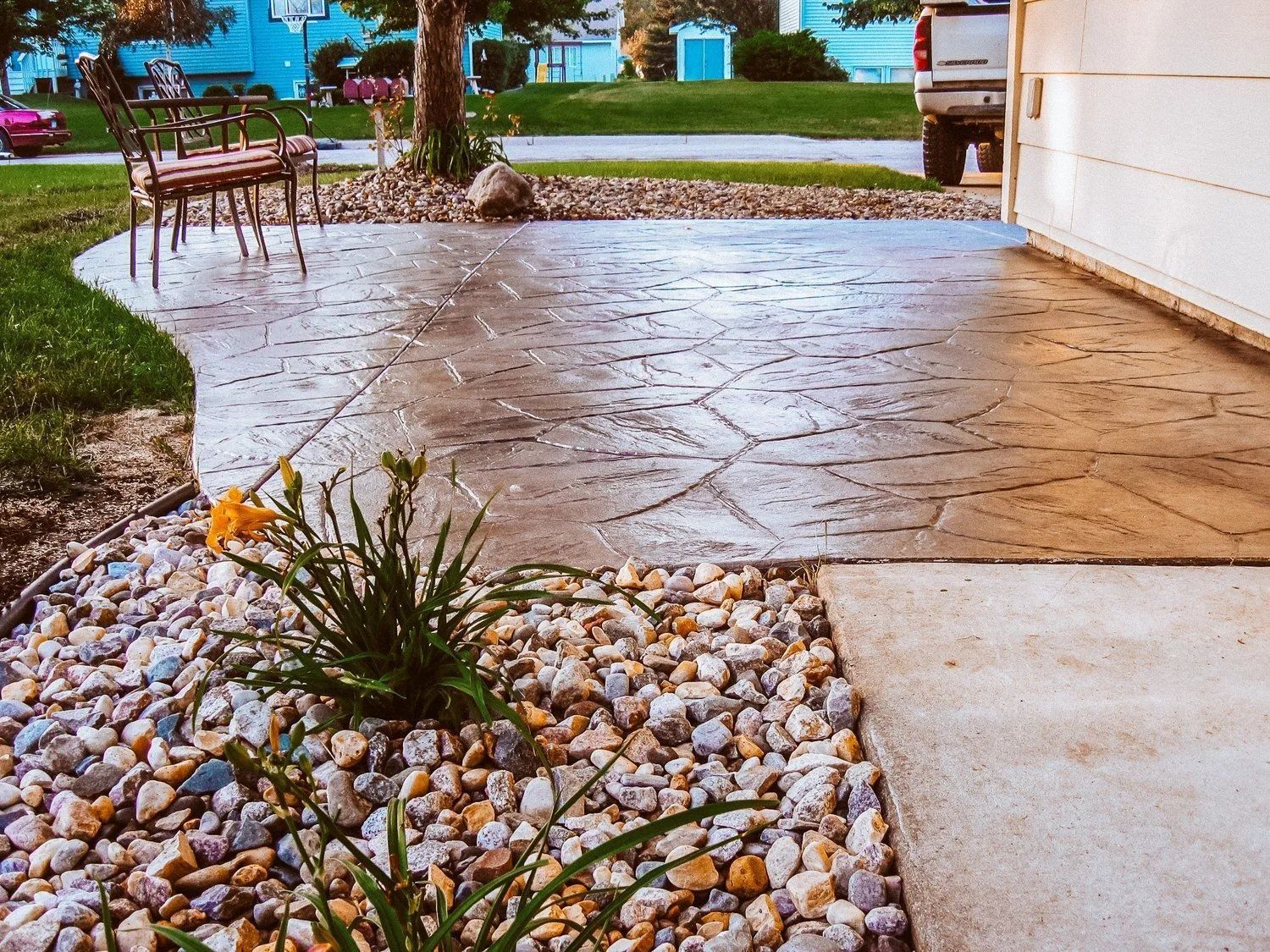 Stamped concrete patio with rock garden, near garage, featuring leaf pattern, and lawn.