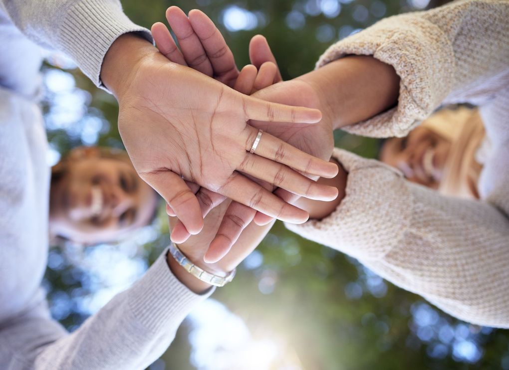 Group of hands stacked together, symbolizing teamwork and unity, seen from a low angle.