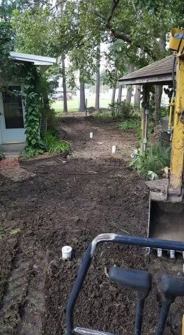 A yellow excavator is digging a hole in the dirt in front of a house.