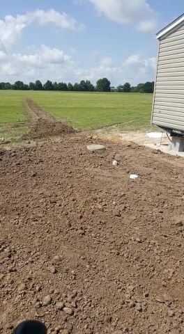 A dirt field with a house in the background and a field in the background.