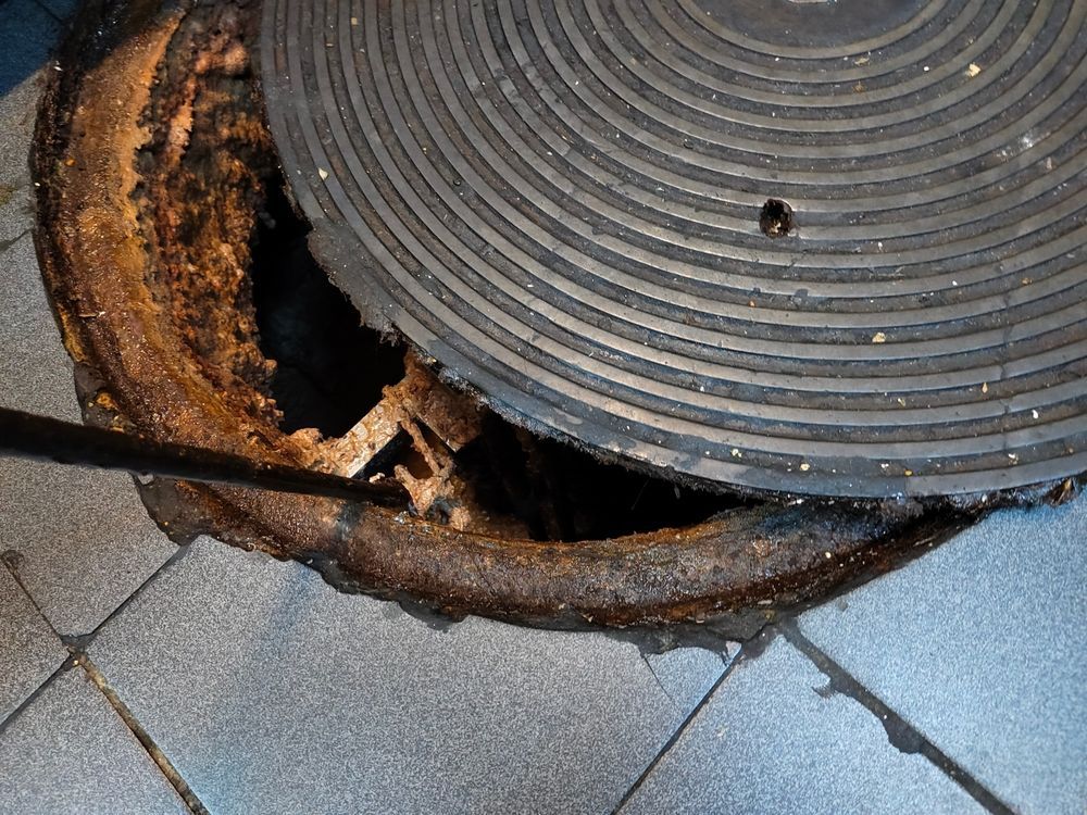 A manhole cover is open on a tiled floor.