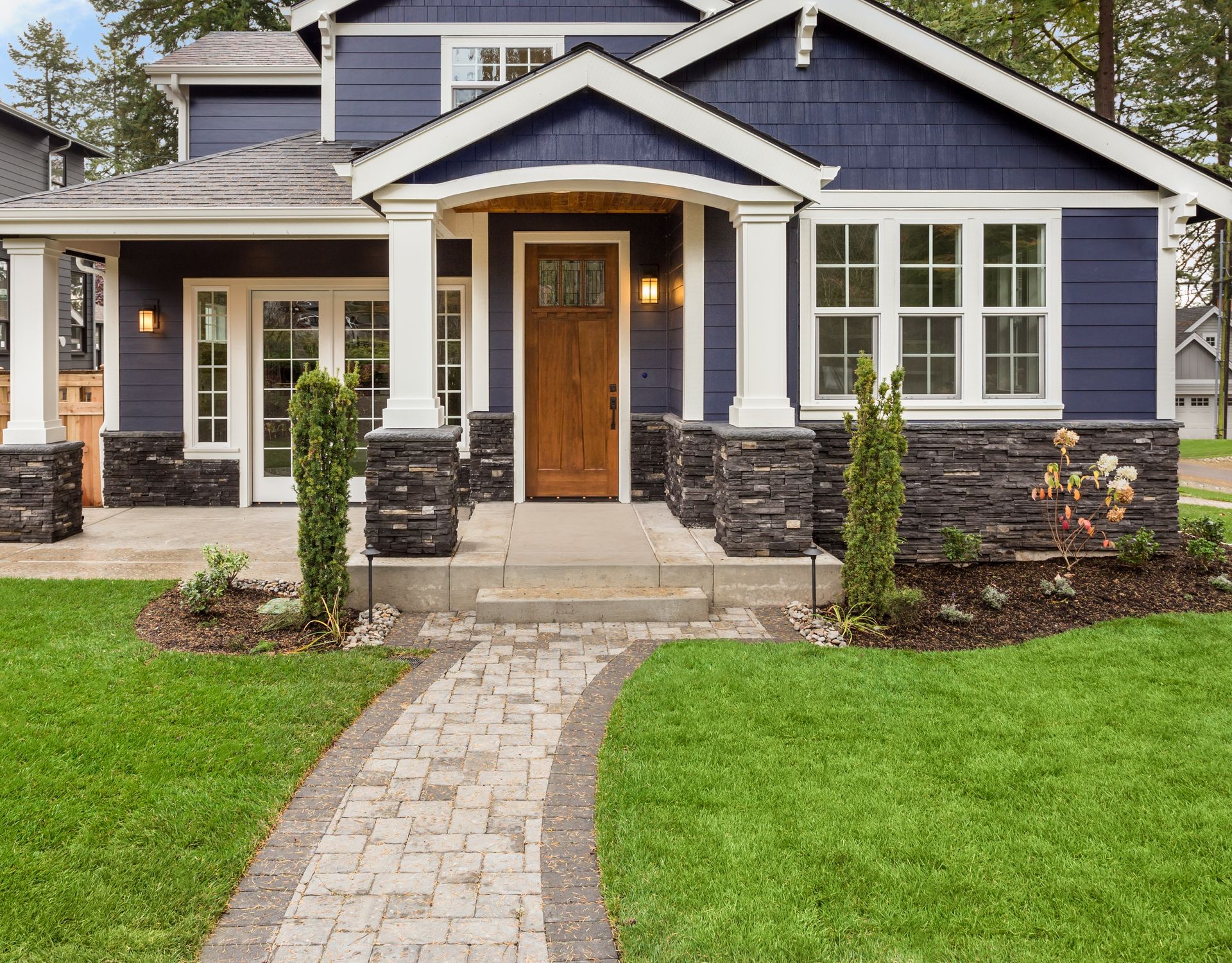 Blue house with stone columns, wooden door, and stone walkway leading to the front porch.