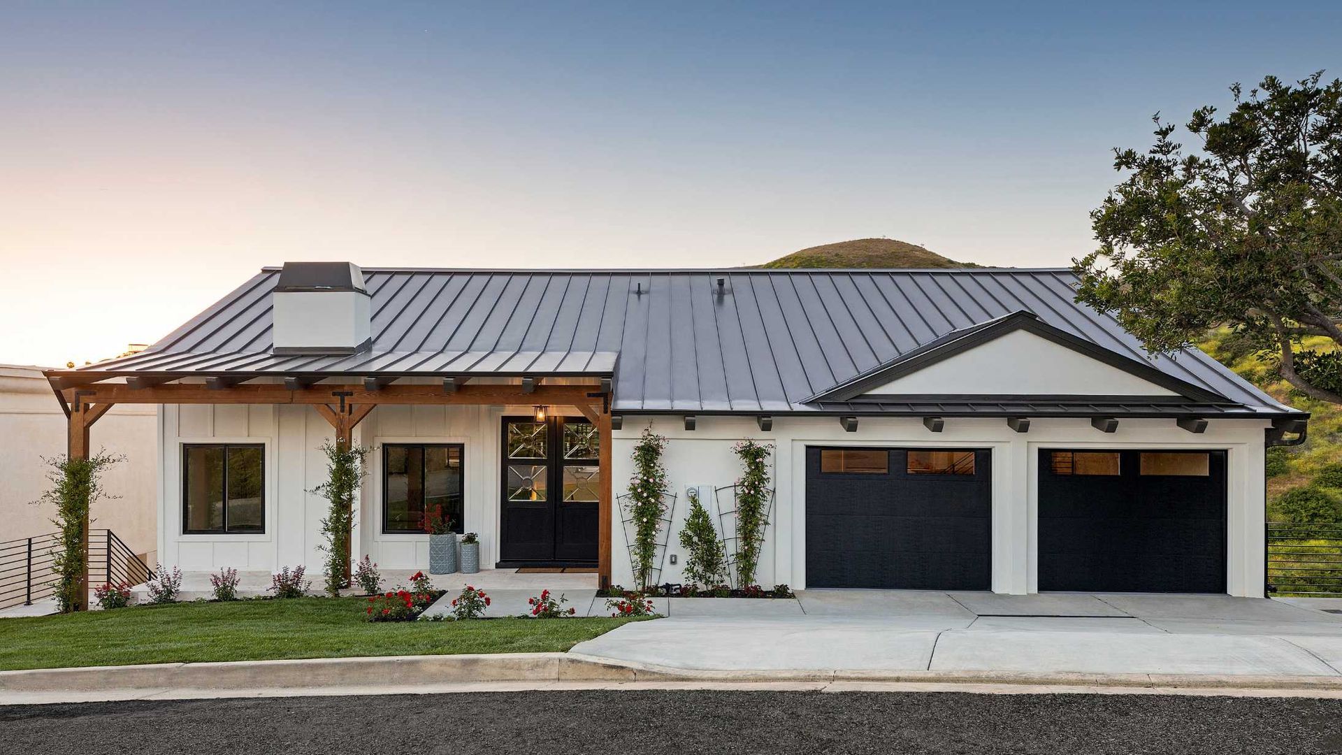 White farmhouse with gray roof and black garage doors.