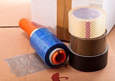 Roll of Plastic Wrap and Three Rolls of Tape Are Sitting on Top of a Cardboard Box — Bargara Removals in Rubyanna, QLD