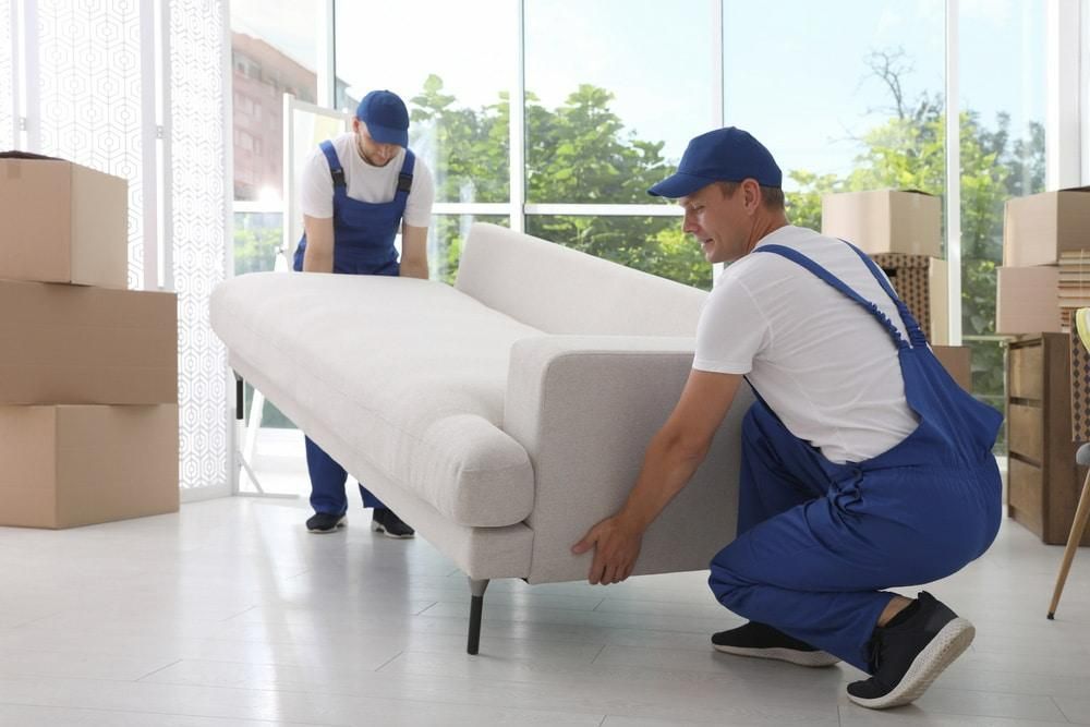 Two Men Are Moving a White Couch in a Living Room — Bargara Removals in Rubyanna, QLD