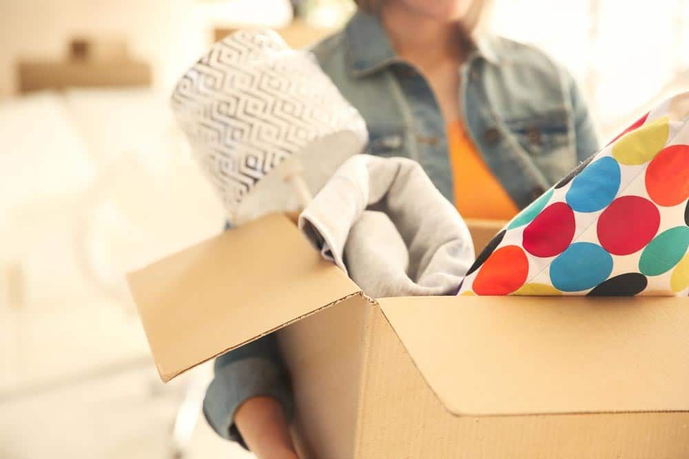 Woman is Holding a Cardboard Box Filled With Clothes — Bargara Removals in Rubyanna, QLD