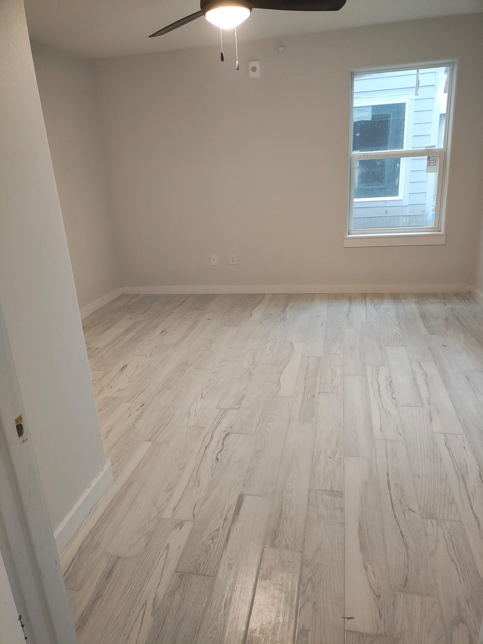 An empty room with a ceiling fan and a window.
