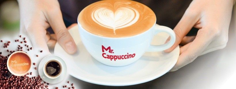 A person is holding a cup of cappuccino on a saucer.