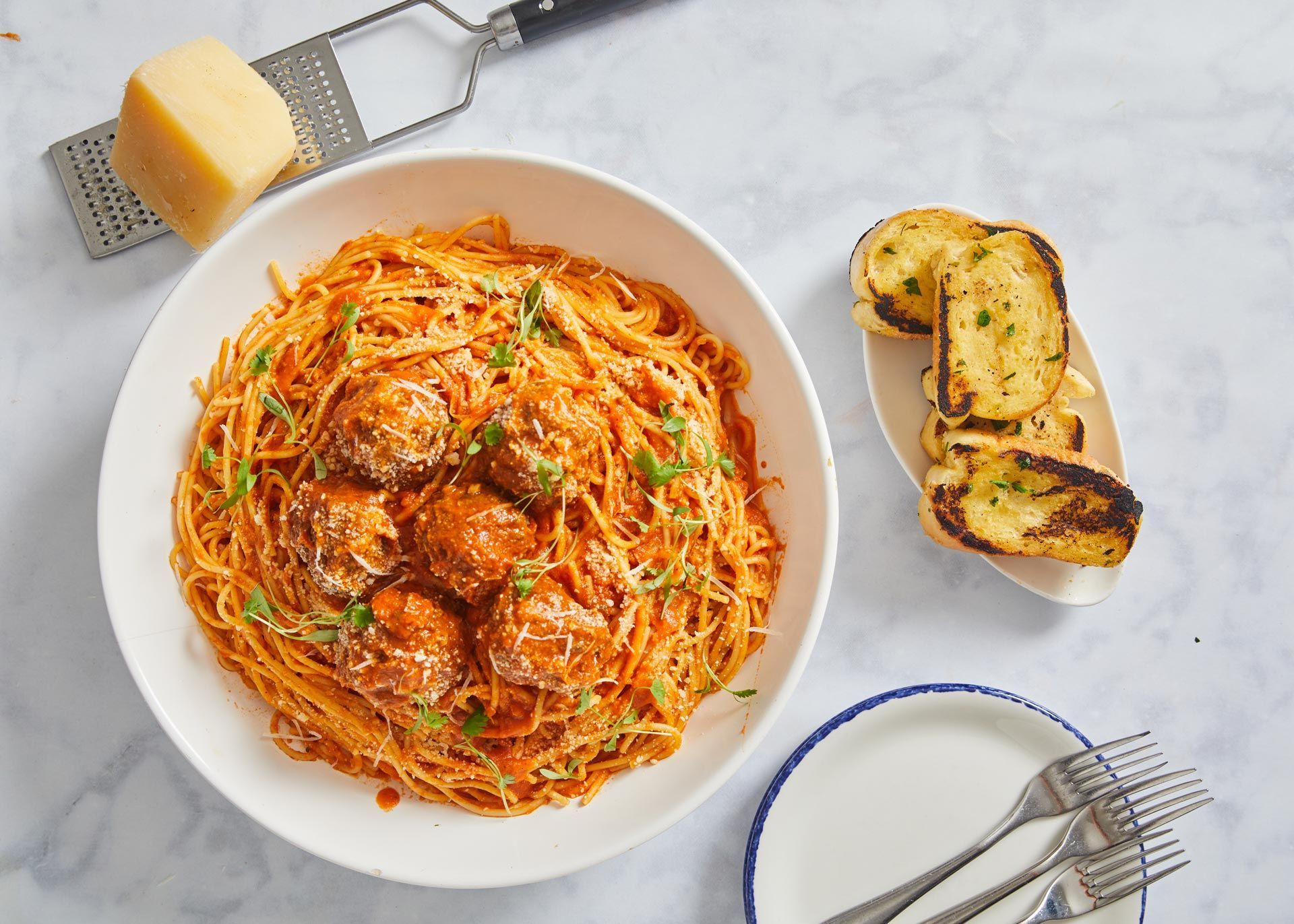 A bowl of spaghetti and meatballs next to a plate of garlic bread.