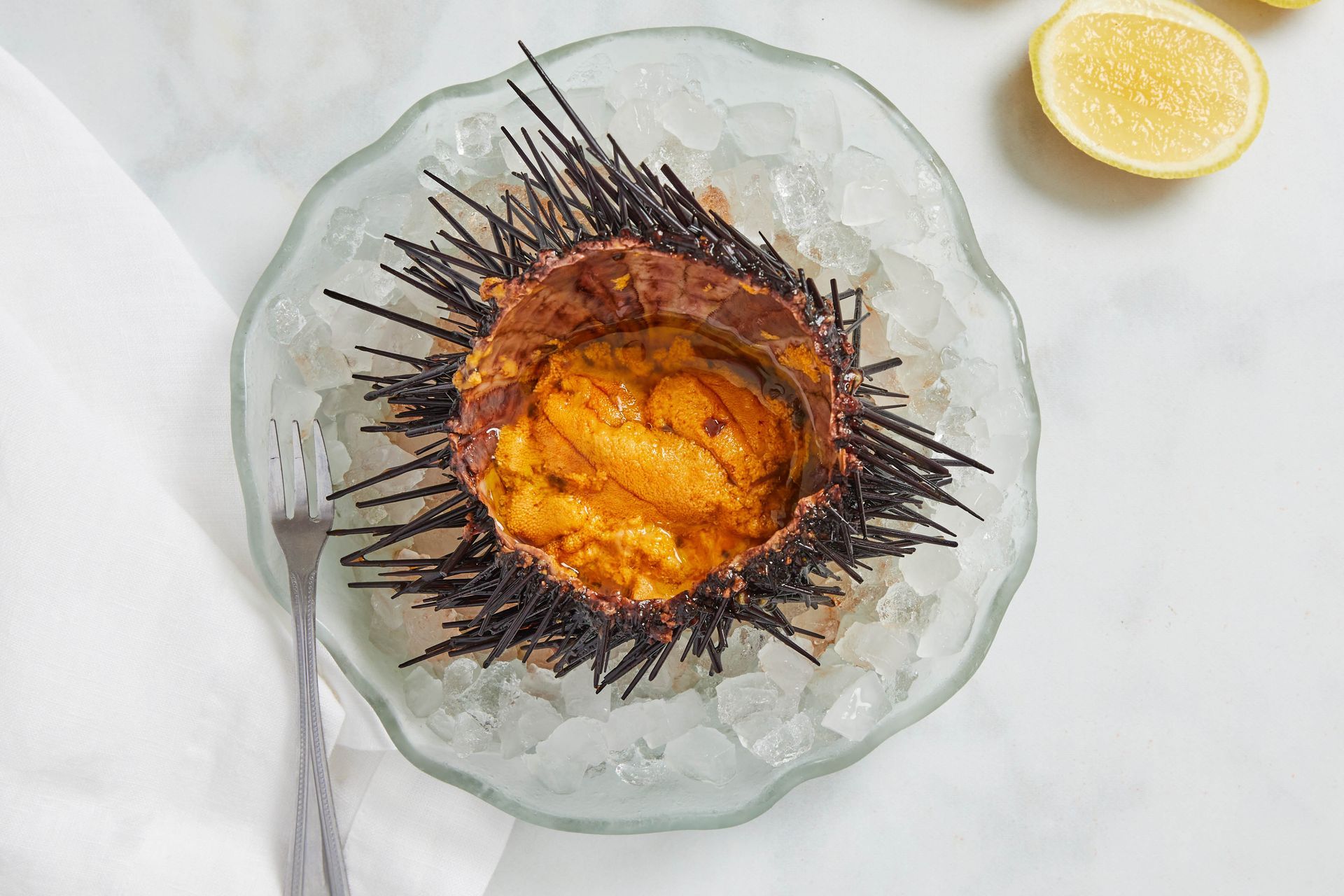 A sea urchin is sitting on ice on a plate with a fork.