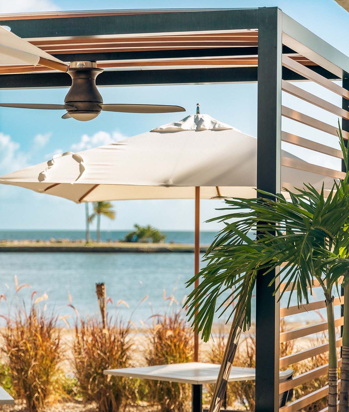 A pergola with umbrellas and a ceiling fan overlooking the ocean
