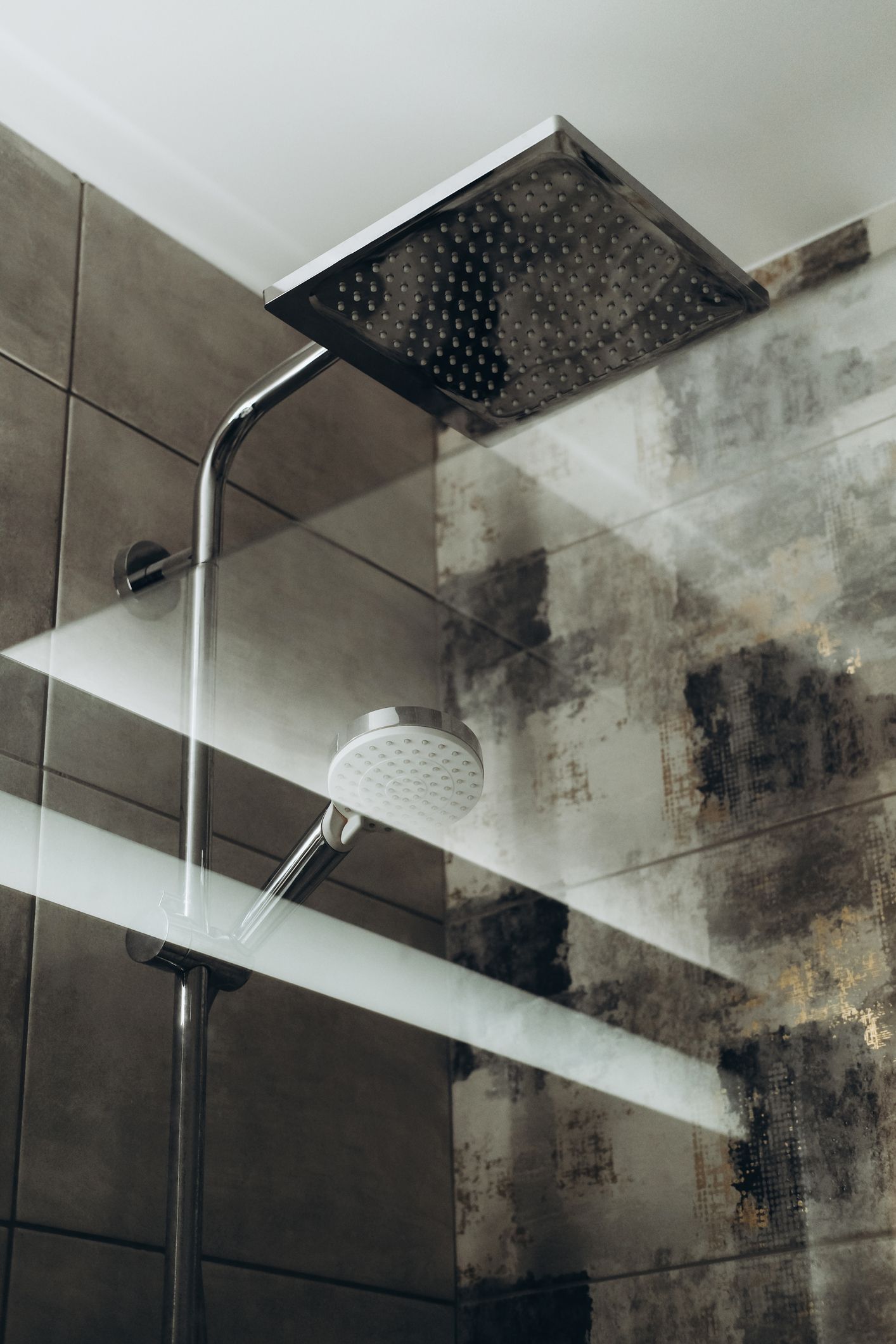Modern shower head in a tiled bathroom with glass partition.
