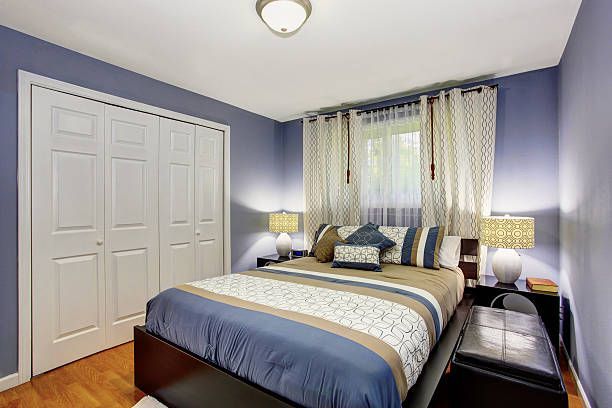 Blue bedroom interior with a bed and white built-in wardrobe.