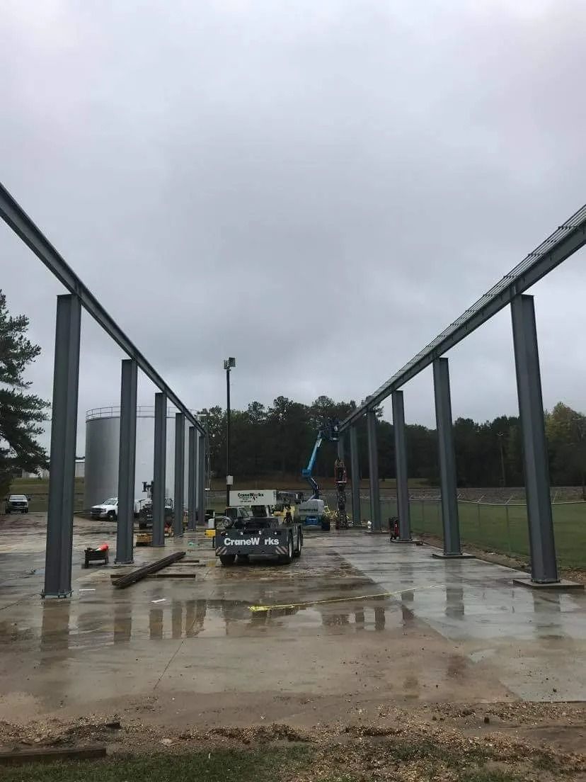 Steel beams being erected for a building on a wet concrete foundation under a cloudy sky.