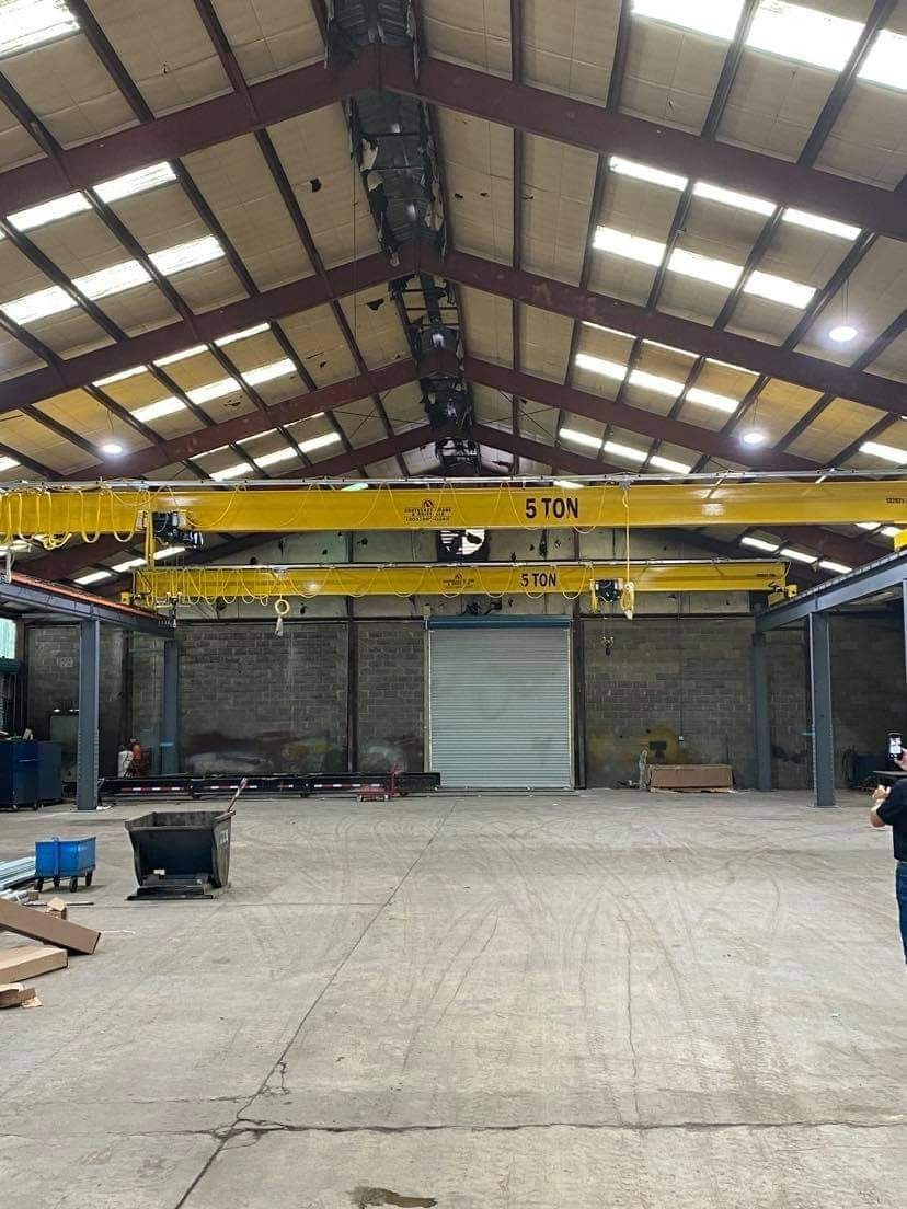 Inside of a warehouse with a yellow overhead crane. A closed roll-up door is centered at the back.