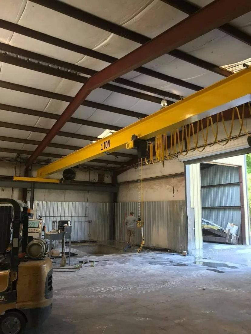 Yellow overhead crane inside a workshop; forklift on the left.