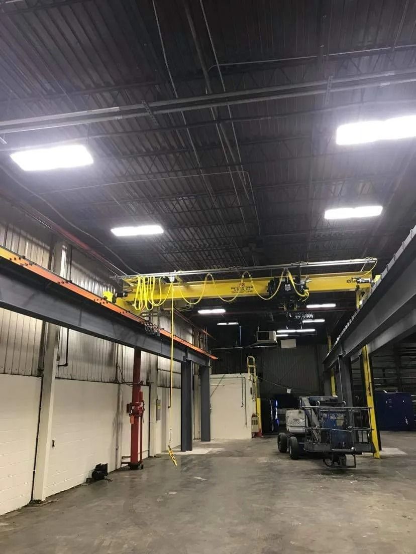 Warehouse interior with overhead crane, white walls, and bright ceiling lights.