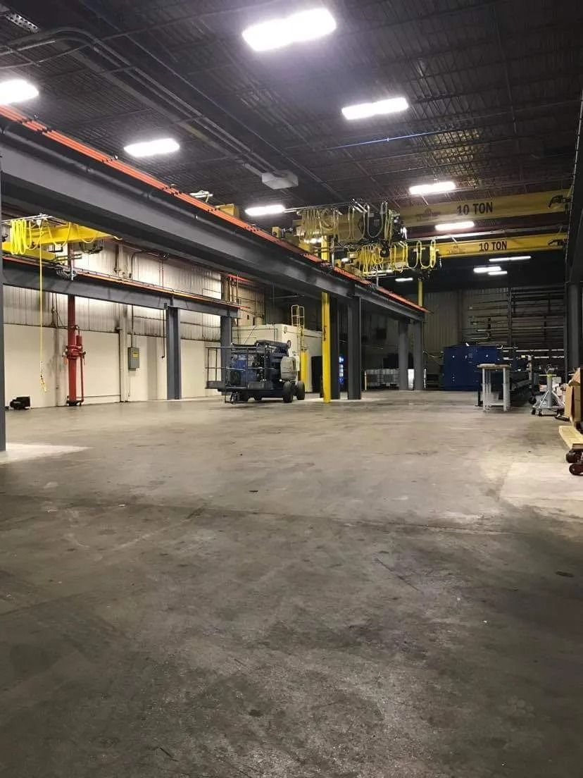 Large industrial warehouse with overhead cranes, concrete floor, and equipment.