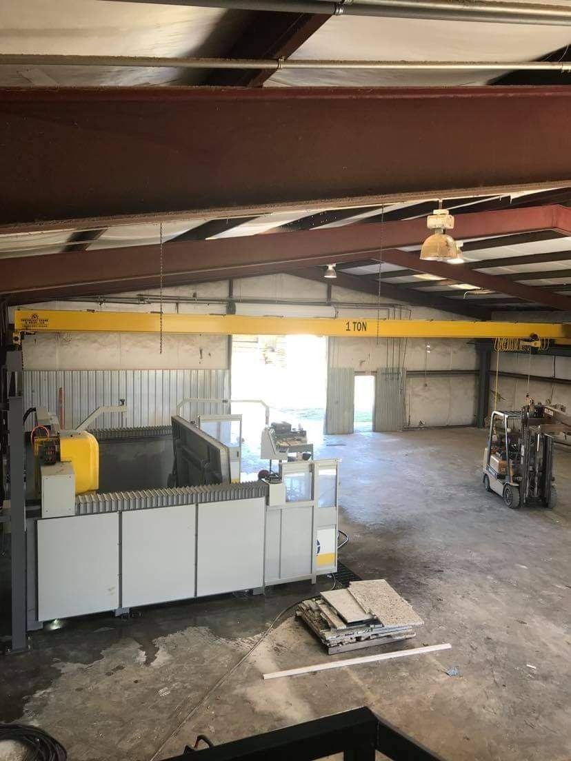 Overhead view of a factory interior with machinery, a crane, and a forklift. The building is gray, white, and yellow.