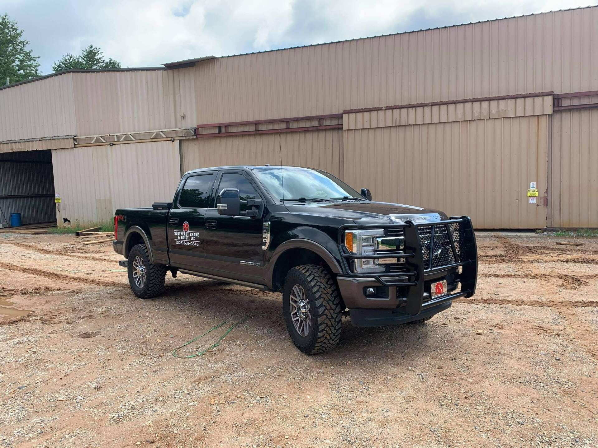 Dark brown pickup truck with a brush guard parked in front of a tan industrial building.