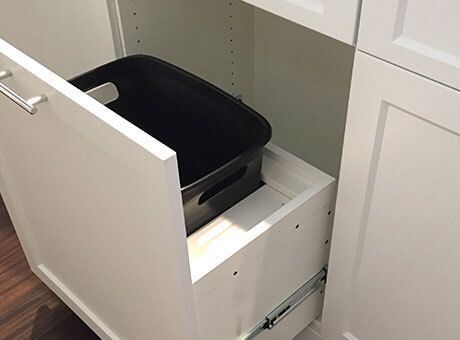 a black trash can is sitting inside of a white drawer .