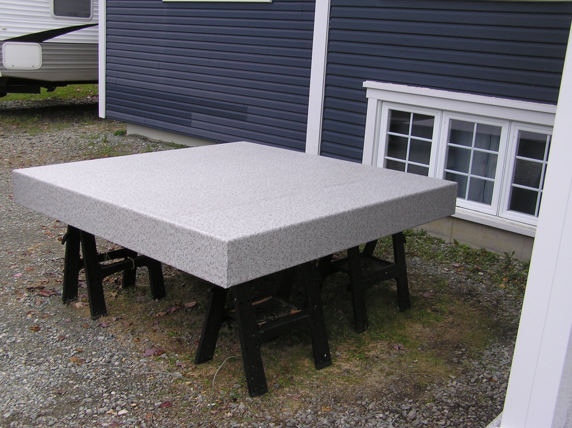 Une plateforme couverte d'une membrane de PVC se trouve devant une maison bleue