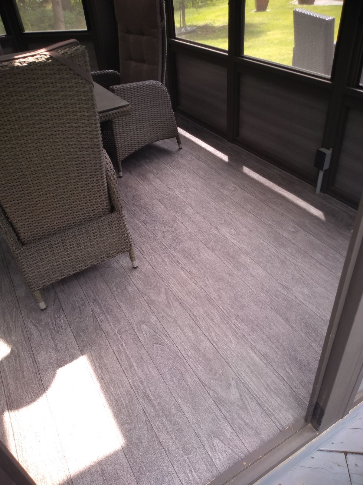 Un porche avec un plancher en membrane de PVC avec des meubles en osier et un tapis.