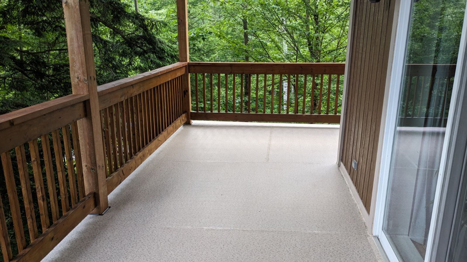 Une terrasse vide avec une balustrade en bois et une porte coulissante en verre.