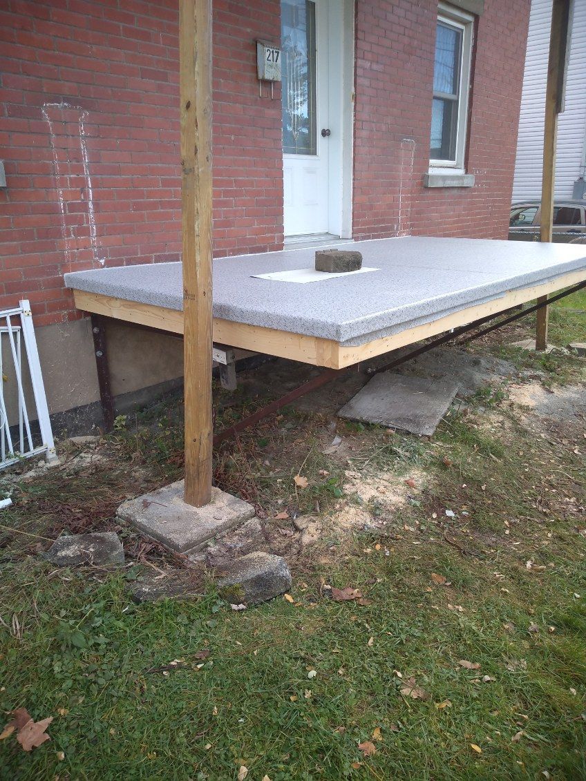 Une terrasse en bois couverte de membrane de PVC est en cours de construction devant une maison en briques.