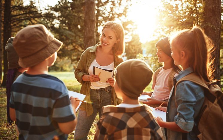 A woman is talking to a group of children in a park.