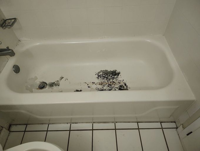 White bathtub with two holes and a white toilet next to it, set in a bathroom with white tiled floor.
