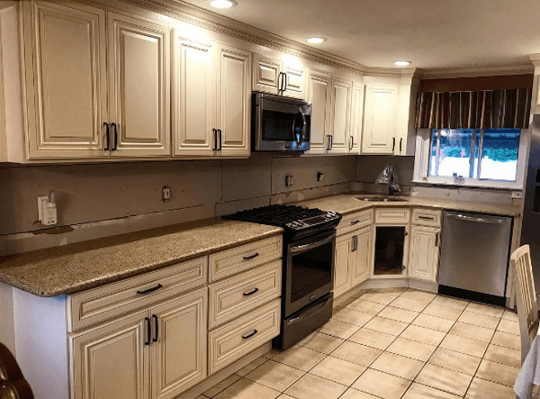 Cream-colored kitchen cabinets and appliances with granite countertops, tile floor and a window.