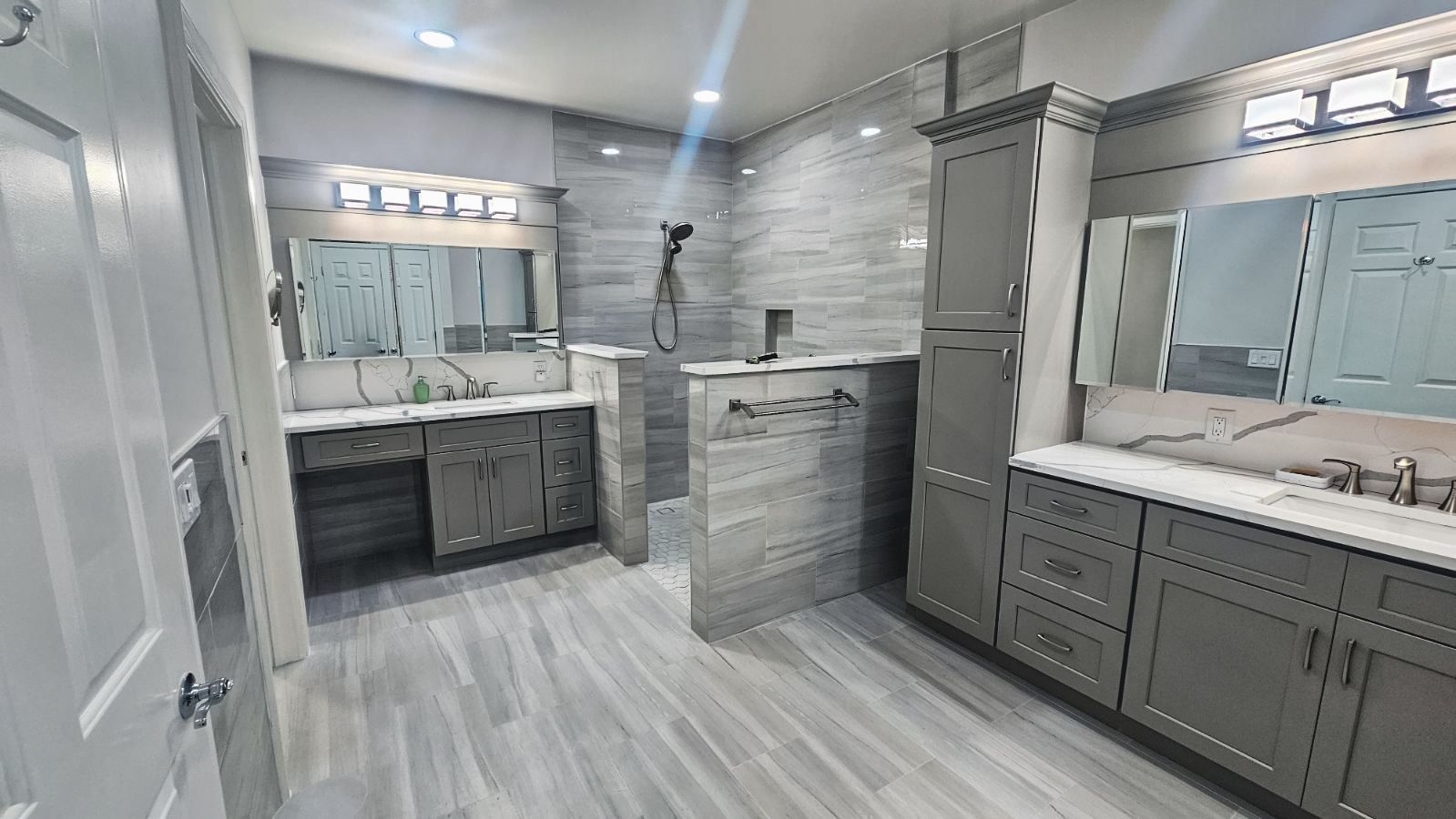 Gray tiled bathroom with dual vanity, shower, and cabinets.