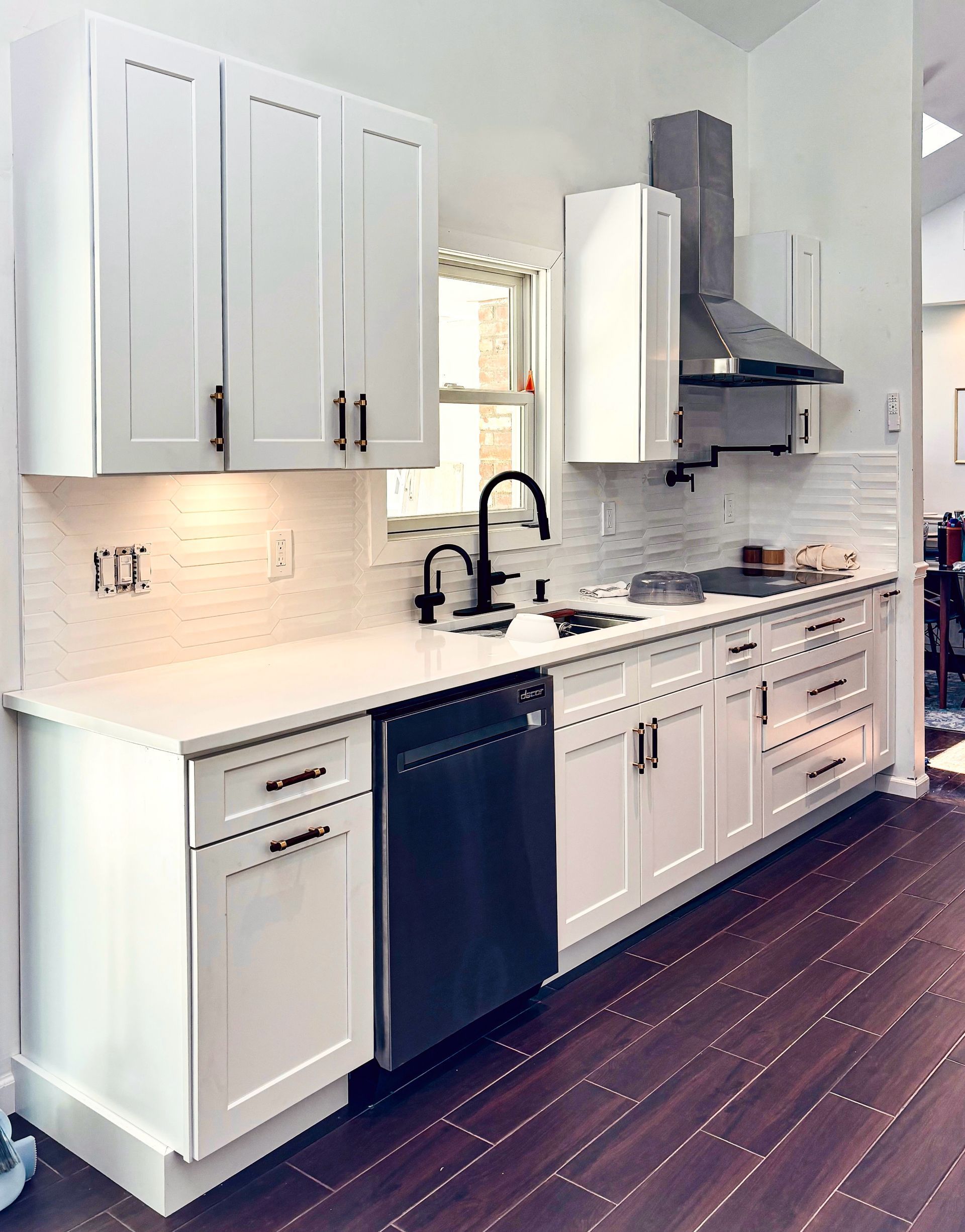 White kitchen with cabinets, black appliances, stainless steel range hood, and wood floors.